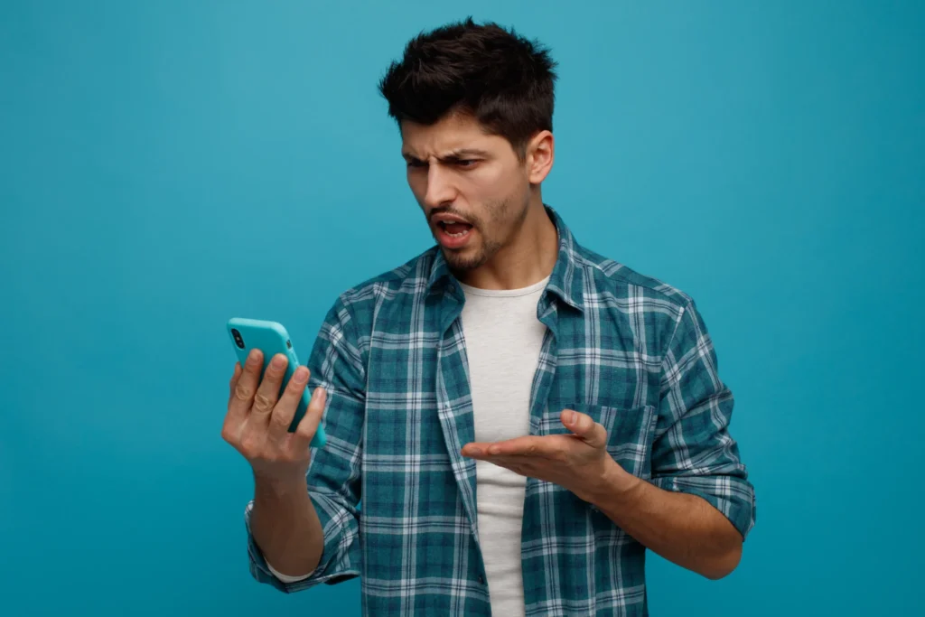 aggressive young man holding looking mobile phone showing empty hand isolated blue background
