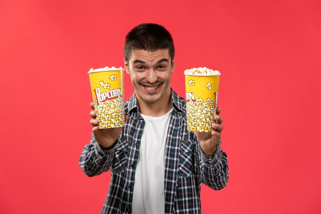 front view young male holding popcorn packages smiling light red wall cinema movie theater film